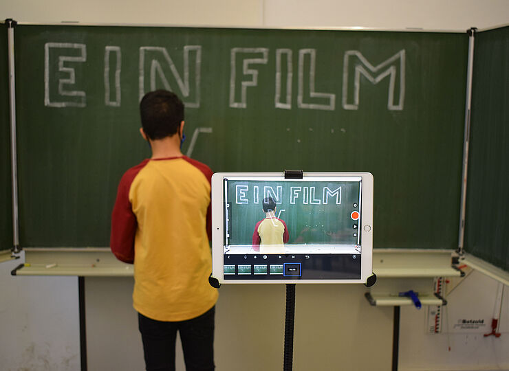 Jugendlicher schreibt an der Tafel und wird dabei mit Tablet gefilmt